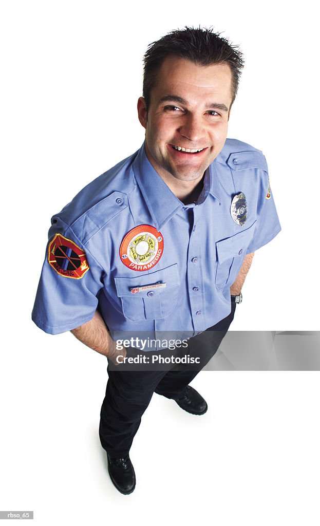 A caucasian male paramedic dressed in uniform stands smiling as he looks up at the camera