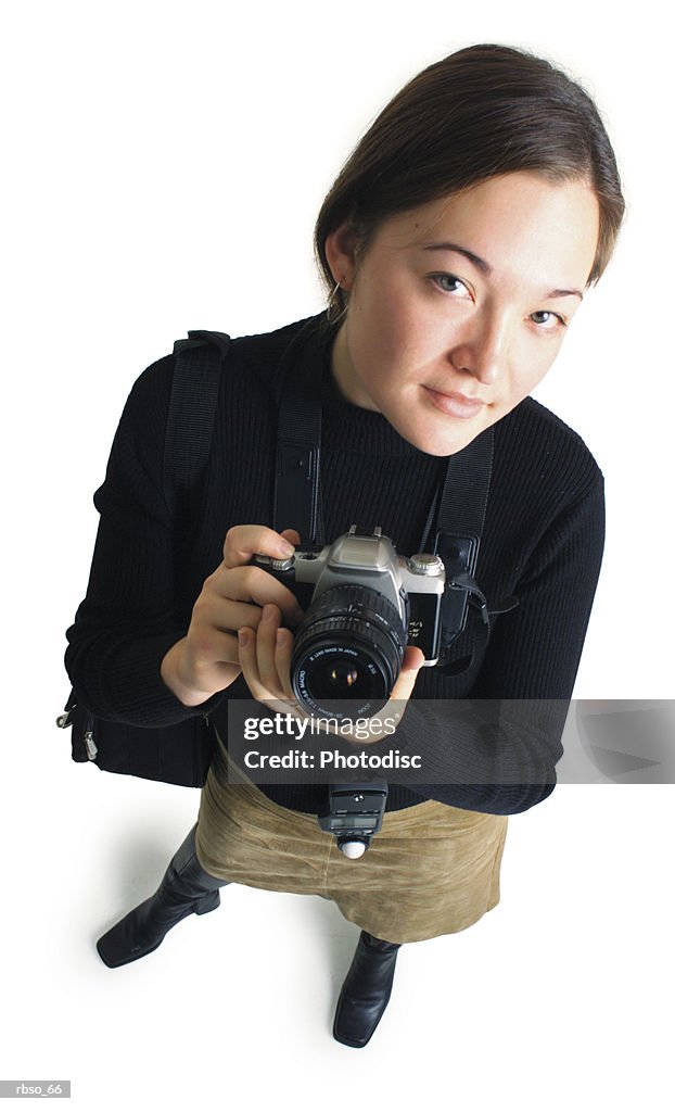 A young ethnic female photographer holds up her camera and looks seriously up at the camera
