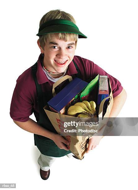 a teenage caucasian male grocery store bagger carries a bag of groceries and looks up at the camera - camera bag stock-fotos und bilder