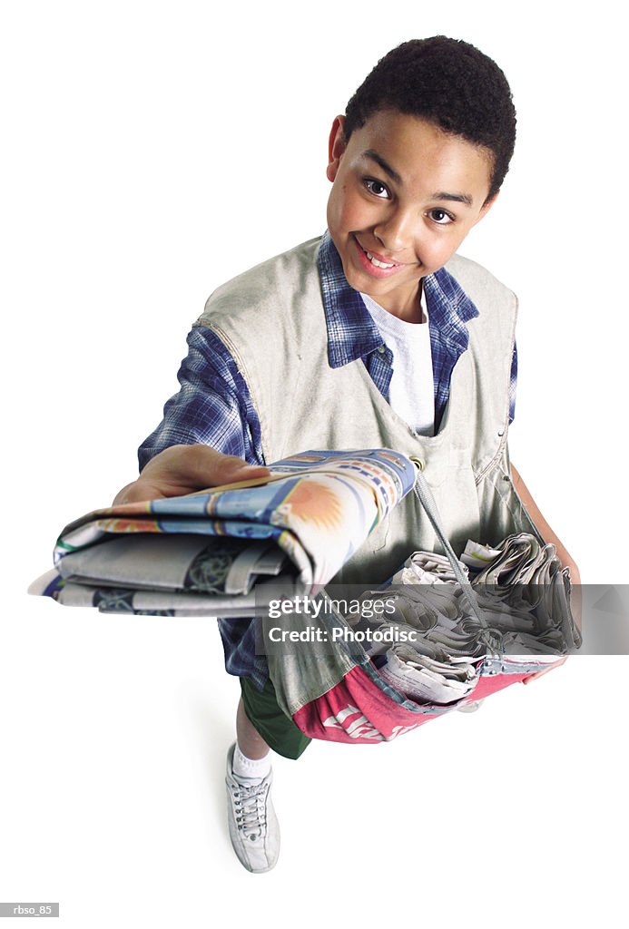 A teenage african american paper boy holds a newspaper up as he smiles up to the camera