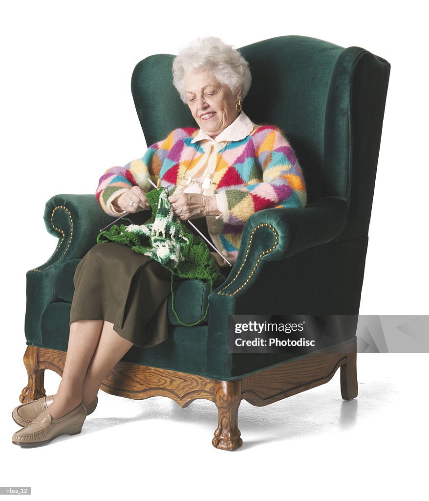 Elderly woman in a colorful sweater knits.