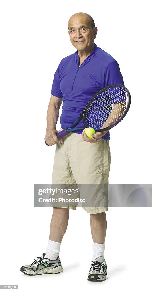 Elderly balding man wearing a blue shirt and holding a tennis racket smiling at the camera.