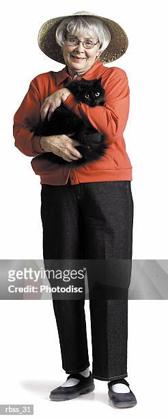 elderly woman in a red shirt and a straw hat smiling at the camera holding a cat - cat with red hat foto e immagini stock