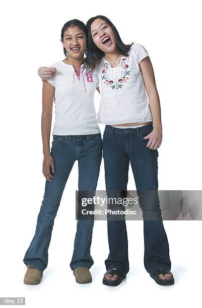 portrait of two asian sisters in jeans and white shirts as they put their arms around each other and smile - smile stockfoto's en -beelden