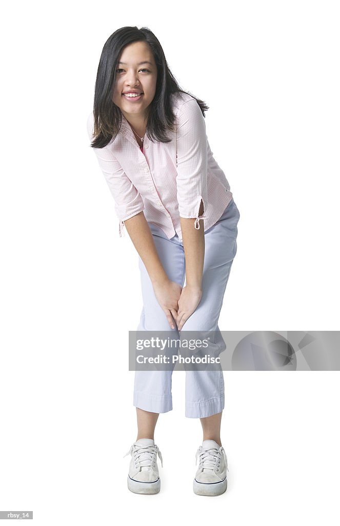 Portrait of an asian female teen in a pink blouse leans in and puts her hands on her knees as she smiles