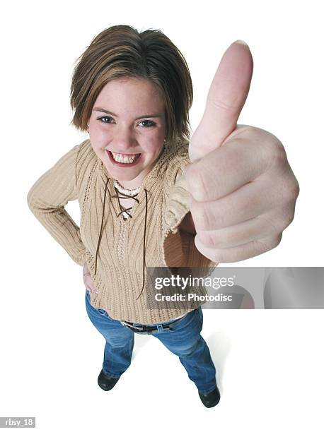 a caucasian teenage girl in jeans and a tan sweater gives the thumbs up sign up into the camera - tan tan stock pictures, royalty-free photos & images