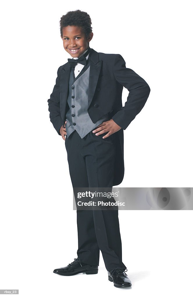 An african american boy dressed in a tuxedo puts his hands on his hips and smiles