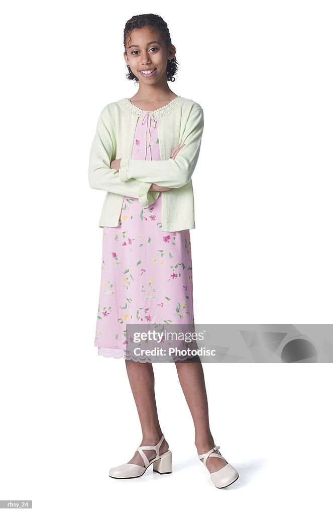 A young african american girl in a pink floral skirt and green sweater folds her arms and smiles