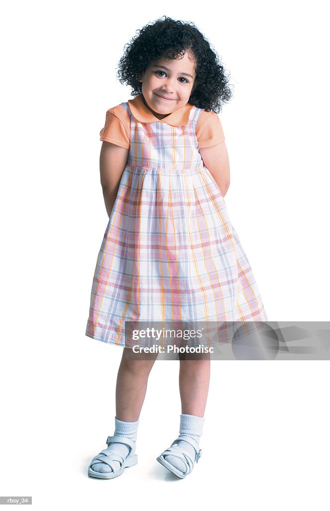 A young african american girl in a plaid dress as she puts her hand behind her back and smiles