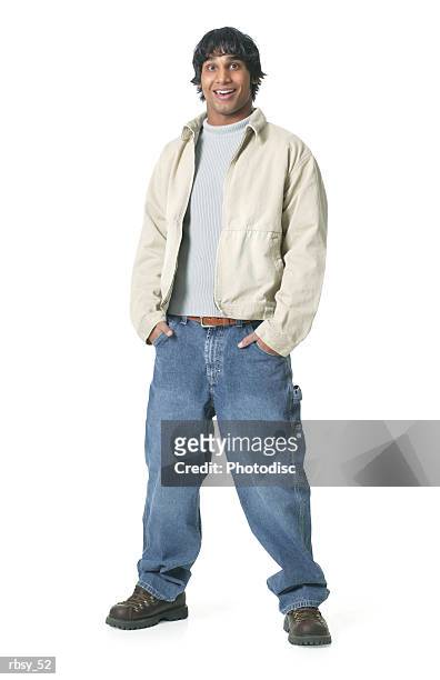 an ethnic teenage male in jeans and a tan jacket puts his hands in his pockets and smiles at the camera - tan tan stock pictures, royalty-free photos & images
