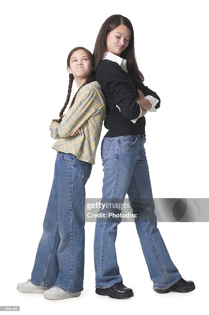 Two young asian sisters fold their arms and stand back to back with their arms folded and looking upset