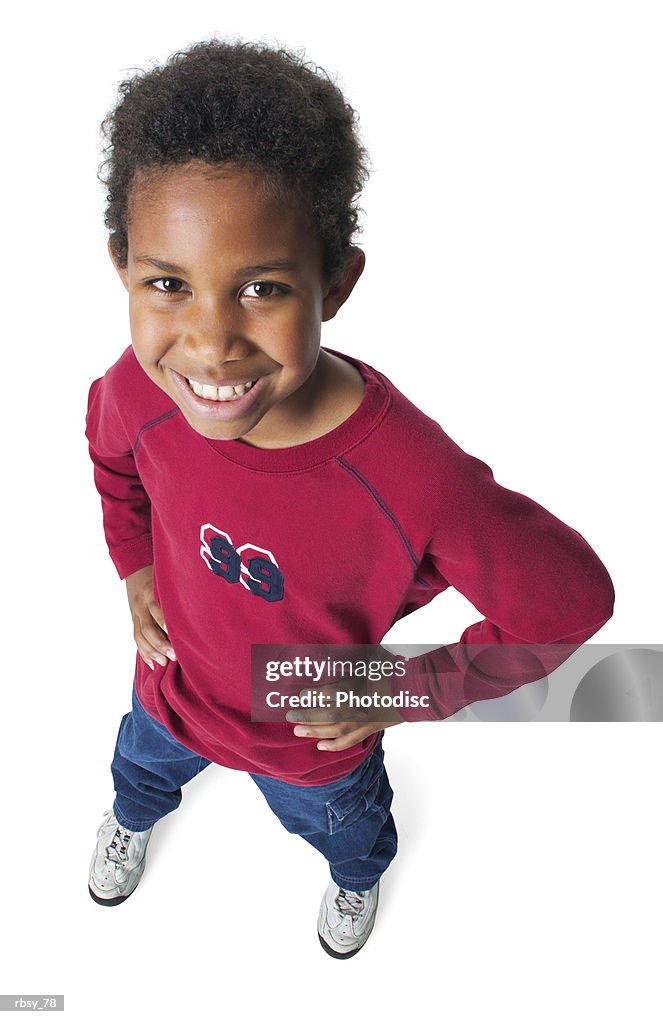 A young african american boy in jeans and a red shirt puts his hands on his hips and smiles up into the camera