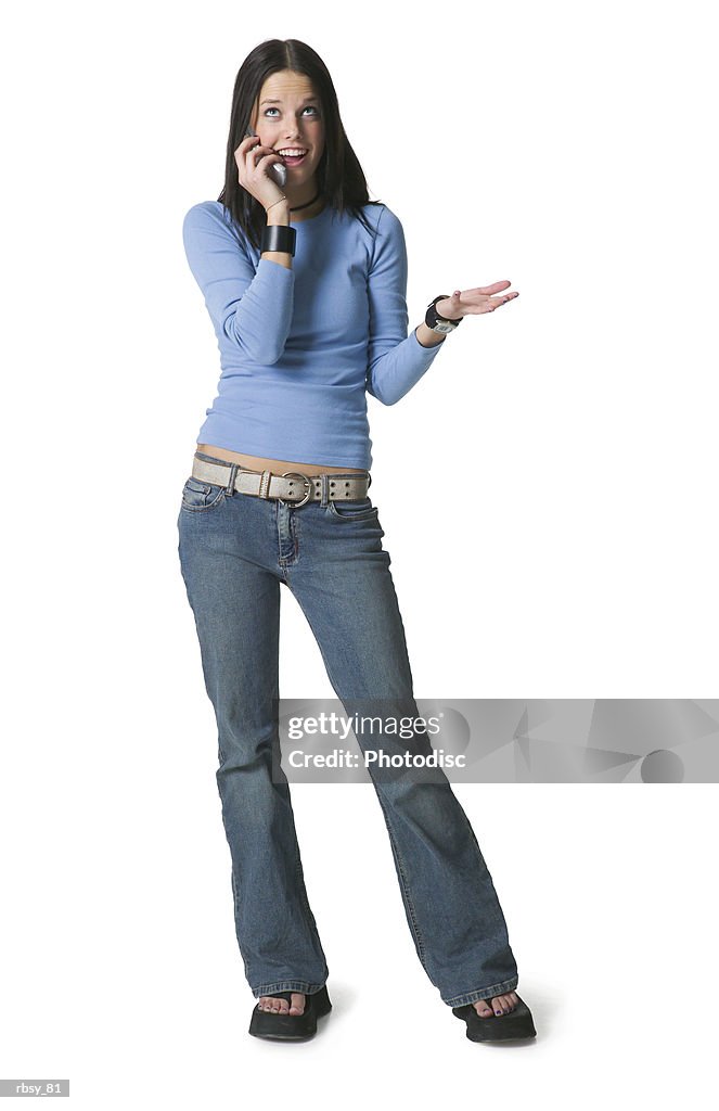 A caucasian female teenager in jeans and a blue shirt chats with a friend on a cell phone