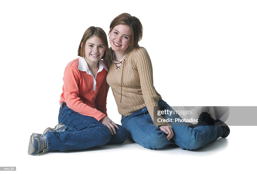 Two young caucasian sisters lovingly sit together and smile