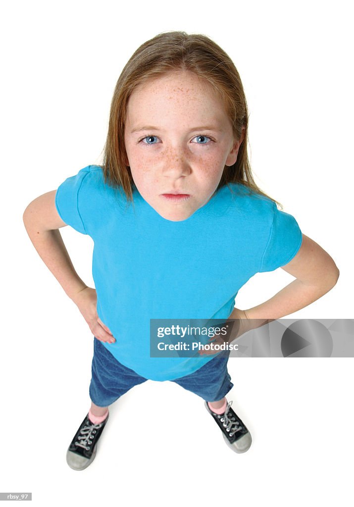 A young caucasian girl in jeans and blue shirt puts her hands on her hips as she frowns up at the camera