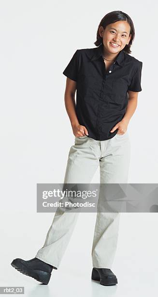 a cute young asian woman stands relaxed with hands in pockets wearing a dark shirt and white slacks - white shirt ストックフォトと画像