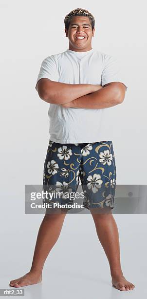 a young smiling hawaiian man with bleached hair wearing flowered shorts and a white teeshirt  stands barefooted with arms folded looking at the camera - short hair photos et images de collection