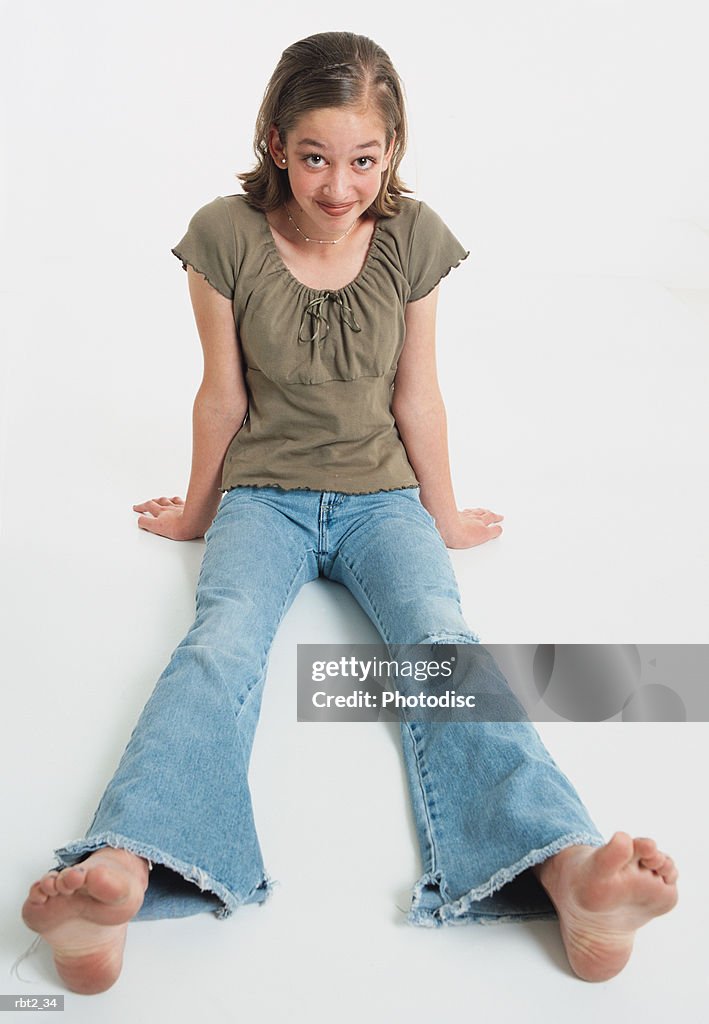 Teenage girl wearing a brown peasant shirt and jeans sits barefoot with her legs spread before her