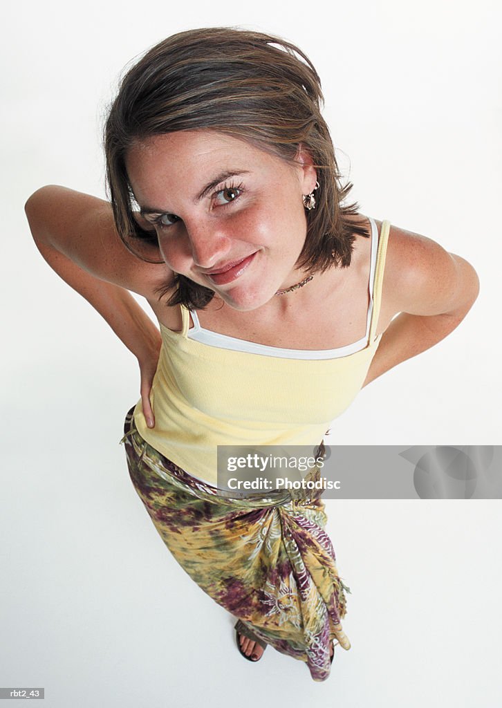 A pretty caucasian young woman in tie dyed skirt and yellow tank top is looking up at the camera with a flirty smile