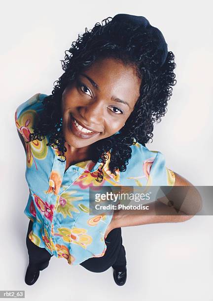 a beautiful african american young woman with curly long hair is wearing a blue floral blouse and smiling up at the camera with her hands on her hips - curly stock pictures, royalty-free photos & images
