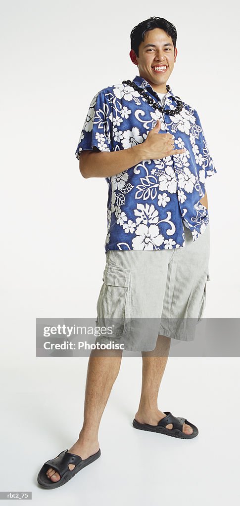 A handsome young latino man in a blue hawaiian shirt and shorts and sandals with a shell necklace gestures in sign language and smiles happily