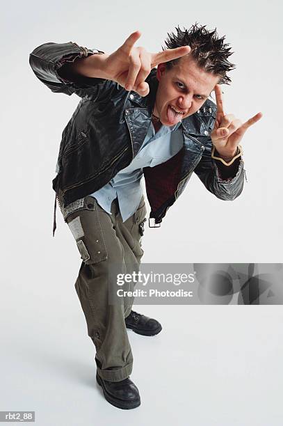 teenage boy spiked hair wears leather jacket stands toward camera gesturing sticks out his tongue - spiky hair stock pictures, royalty-free photos & images