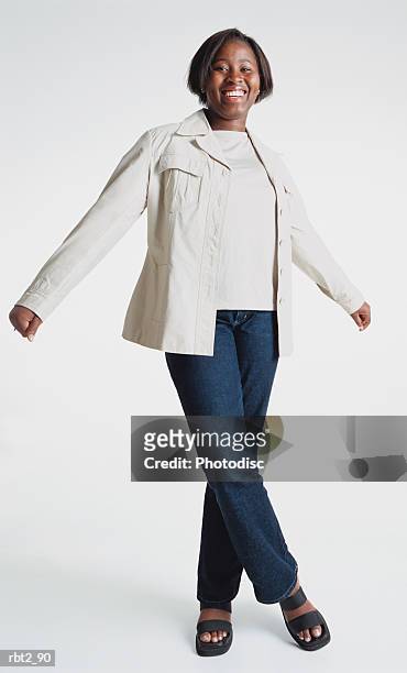 a cute african american teenage girl wearing jeans and a white blazer is standing about to twirl around as she spreads her arms and one foot crosses over the other - about stock pictures, royalty-free photos & images