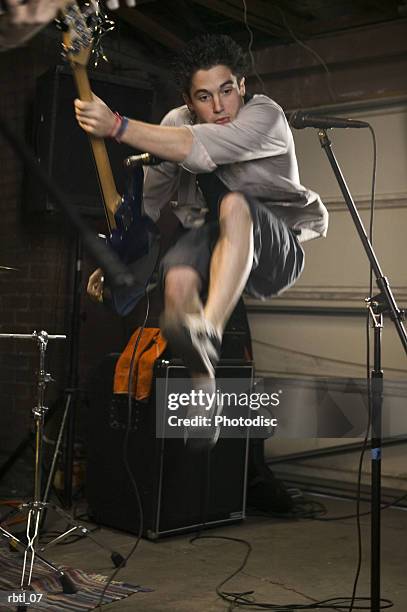 lifestyle portrait of a teenage male as he jumps up through the air while playing his guitar - rock moderne photos et images de collection