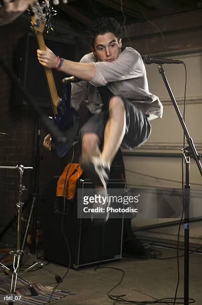 lifestyle portrait of a teenage male as he jumps up through the air while playing his guitar - modern rock stock pictures, royalty-free photos & images