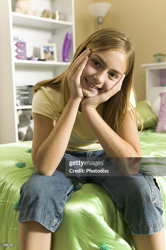 Lifestyle portrait of a teenage female in a yellow shirt as she sits on her bed and smiles