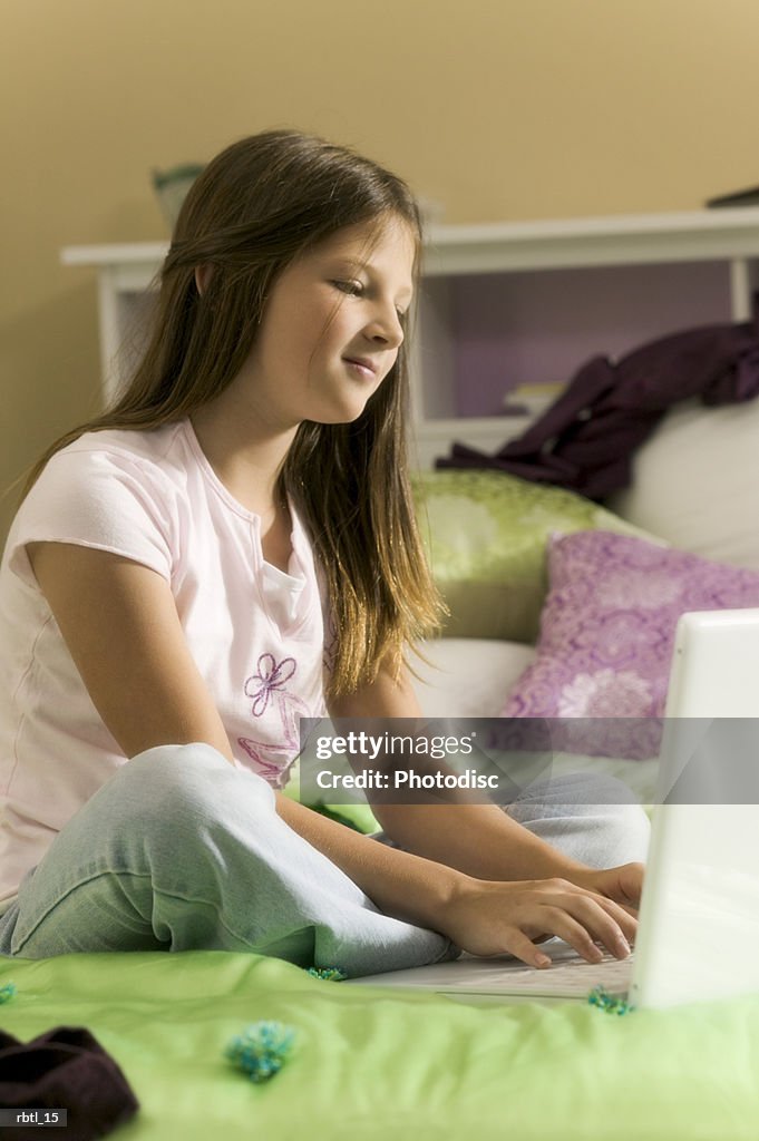 Lifestyle portrait of a teenage female as she sits on her bed and uses her computer