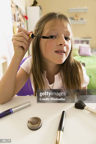 lifestyle portrait of a teenage female as she looks in the mirror to put on eye shadow - make up ストックフォトと画像