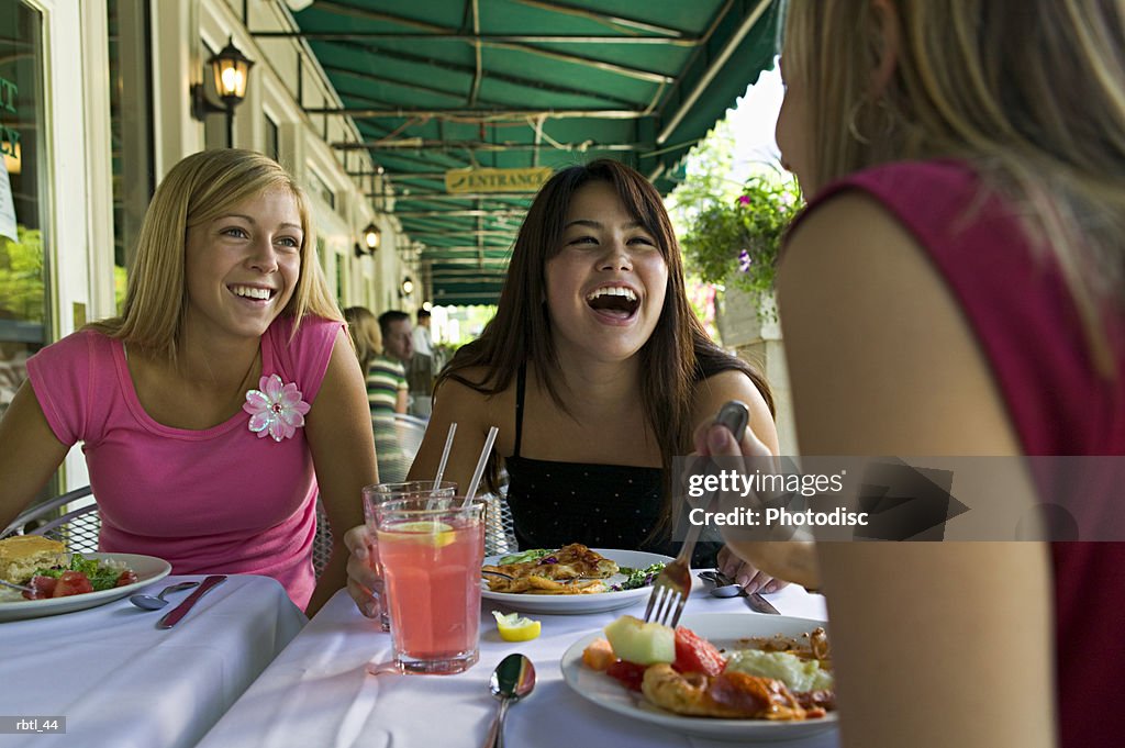 Lifestyle portrait of a group of three teenage female friends as they eat at a sidewalk cafe