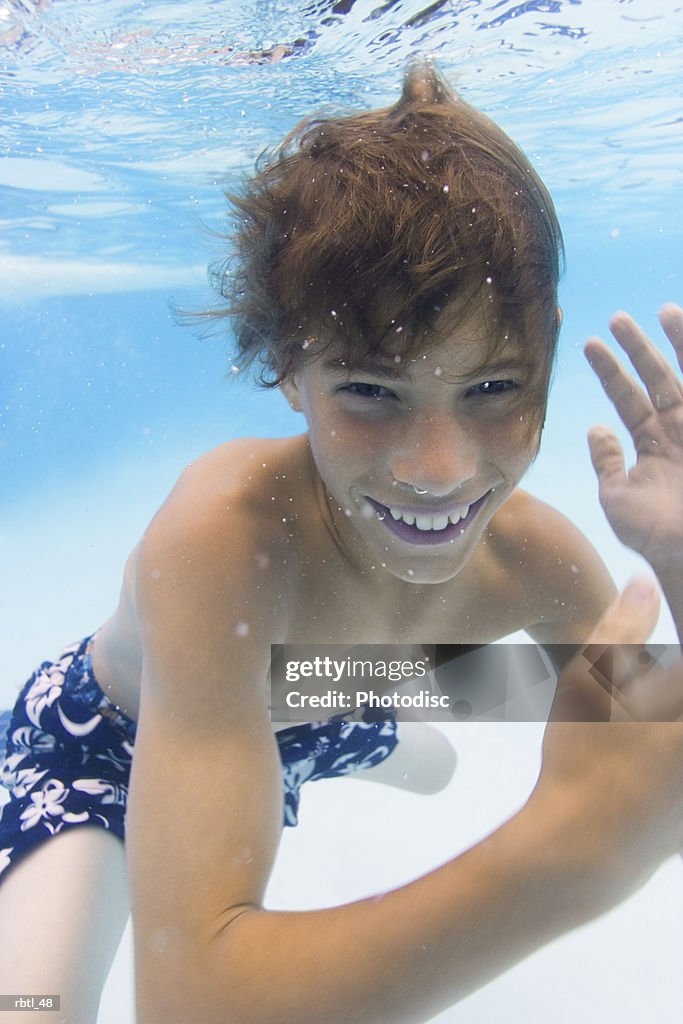 Underwater lifestyle shot of a teenage male as he swims and waves to the camera