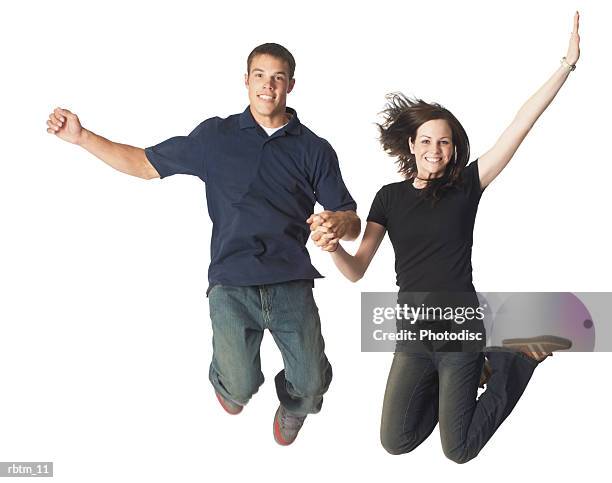 a caucasian teen couple hold hands as they jump up playfully and smile - smile imagens e fotografias de stock