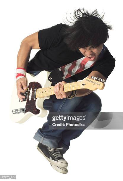 an asian male teen in jeans and a black shirt jumps up while playing an electric guitar - modern rock stock pictures, royalty-free photos & images