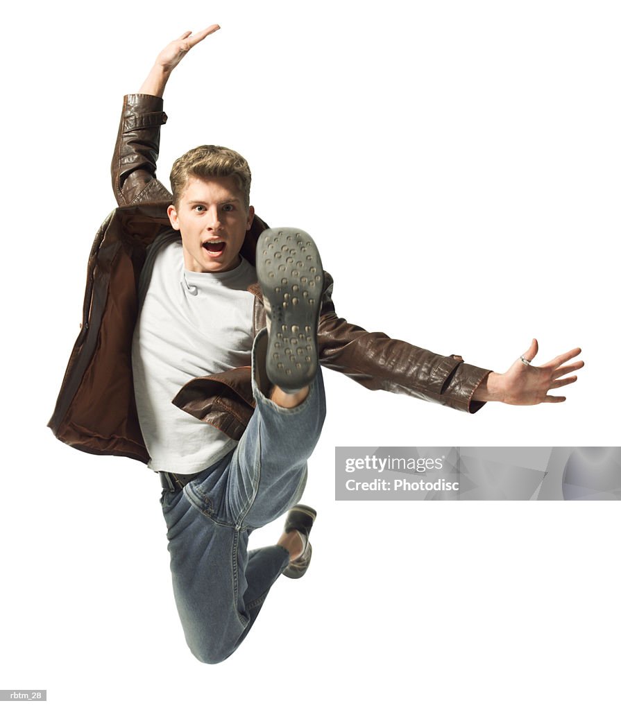 A caucasian male teen in jeans and a leather jacket jumps up playfully