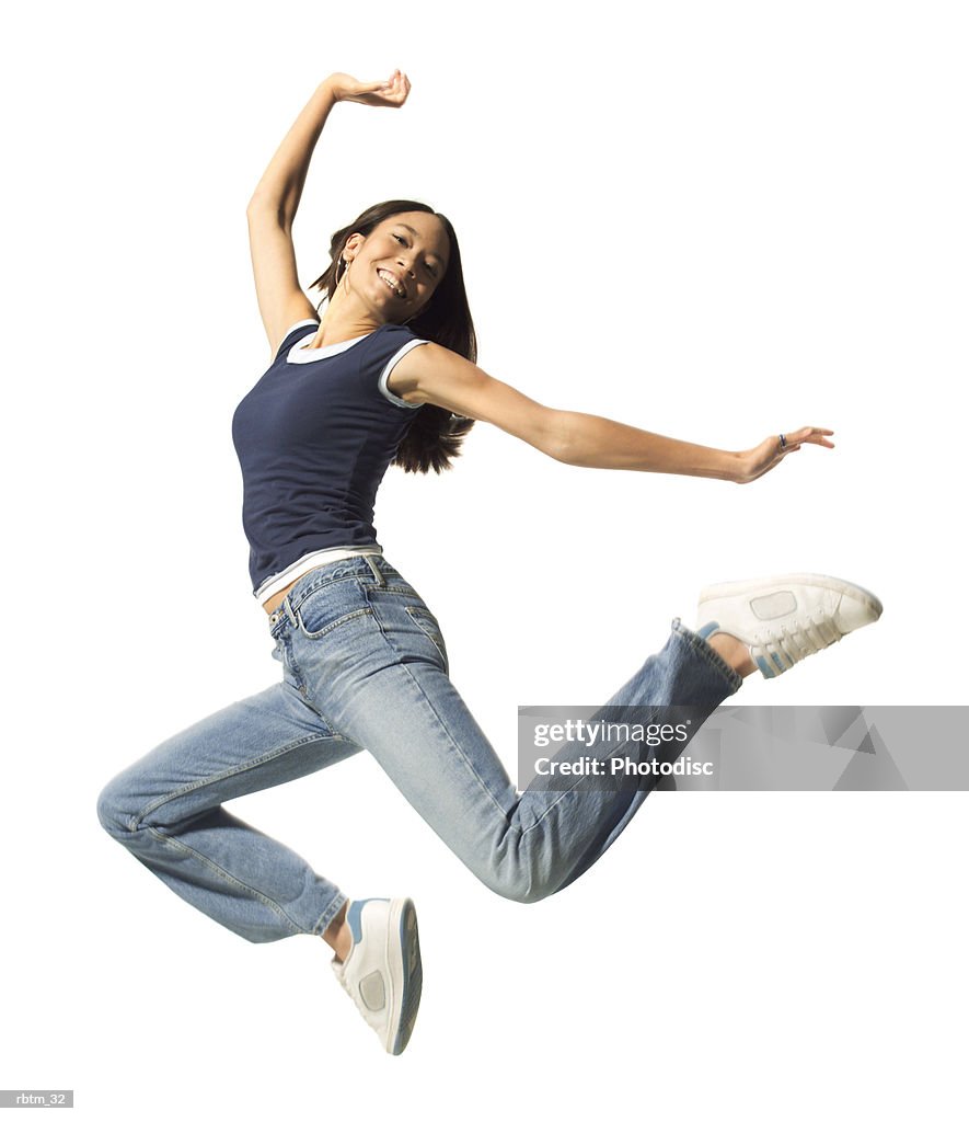 An ethnic teenage female in jeans and a blue tank top jumps up playfully in the air