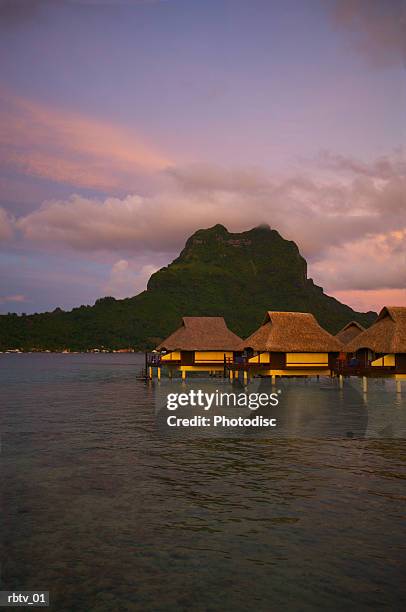 landscape photograph of a tropical resort with huts over the water at sunset - grashut stockfoto's en -beelden