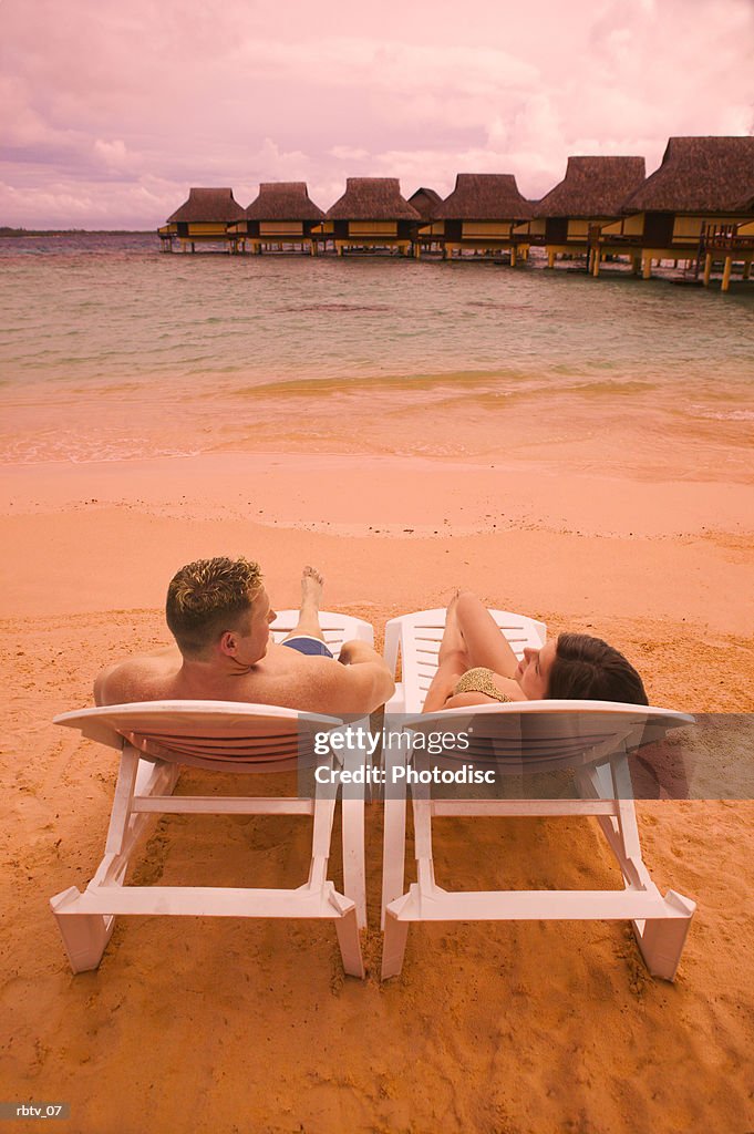 A caucasian couple sit in beach chairs as they overlook a beautiful beach resort in the tropics