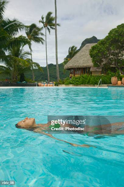 an attractive caucasian woman floats on her back in a swimming pool at a tropical resort - grashut stockfoto's en -beelden