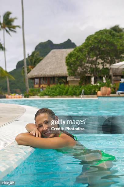 an attractive caucasian woman leans against the edge of a swimming pool at a tropical resort - grashut stockfoto's en -beelden