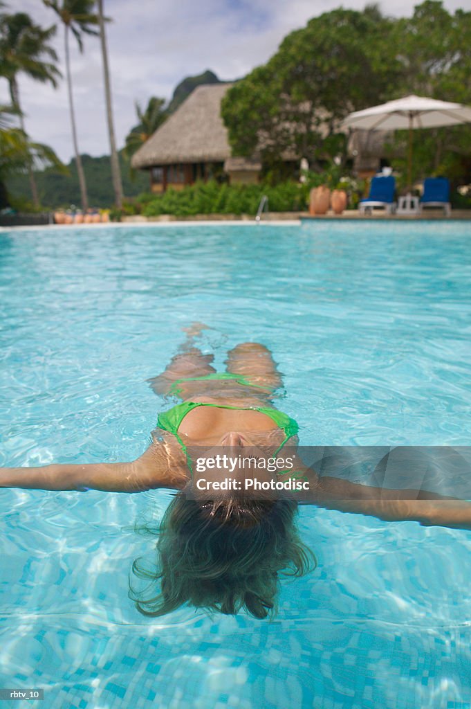 An attractive caucasian woman floats on her back in a swimming pool at a tropical resort