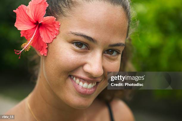 an attractive ethnic woman with a red flower in her hair smiles at the camera - tahiti flower stock pictures, royalty-free photos & images