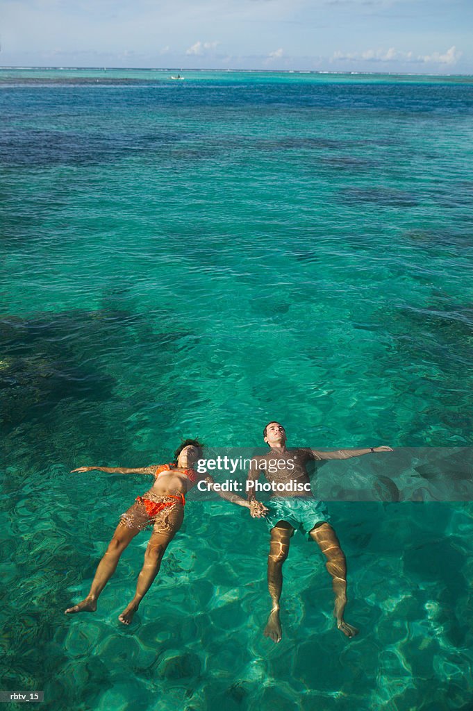 A caucasian couple float on their backs through the clear water of the tropics