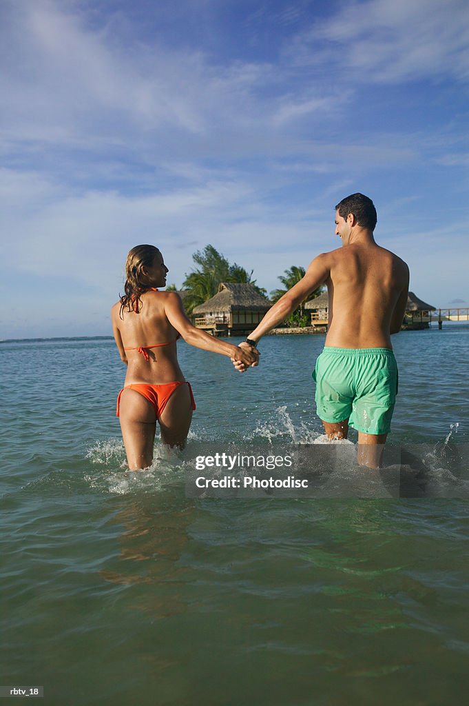 A caucasian couple hold hands and run through the water as they vacation in a tropical setting