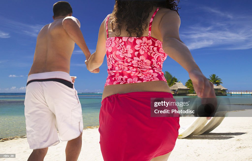 An ethnic couple in swimsuits run along a beautiful beach hand in hand
