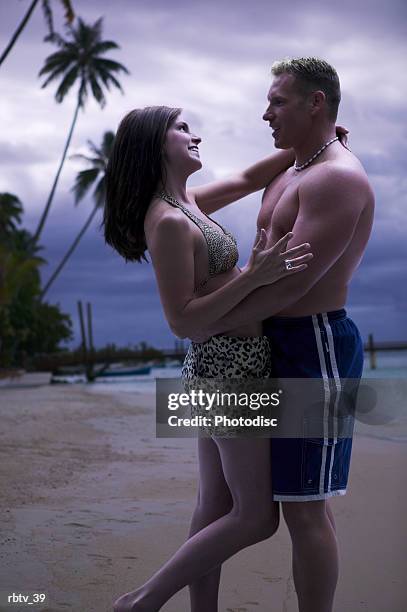 a caucasian couple stand on a beach at sunset as they hug and smile - smile stock-fotos und bilder