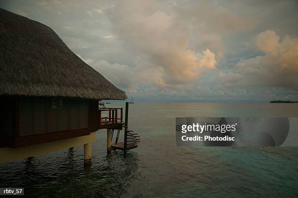 landscape photograph of a grass hut over the water as a tropical storm gathers in the background - grashut stockfoto's en -beelden