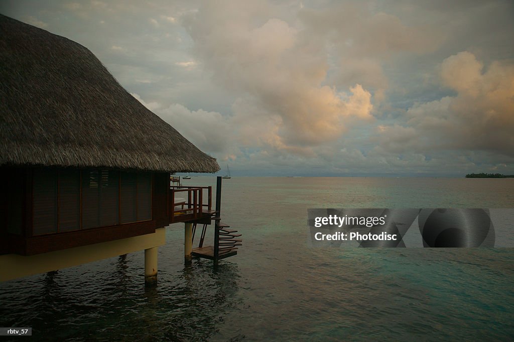 Landscape photograph of a grass hut over the water as a tropical storm gathers in the background